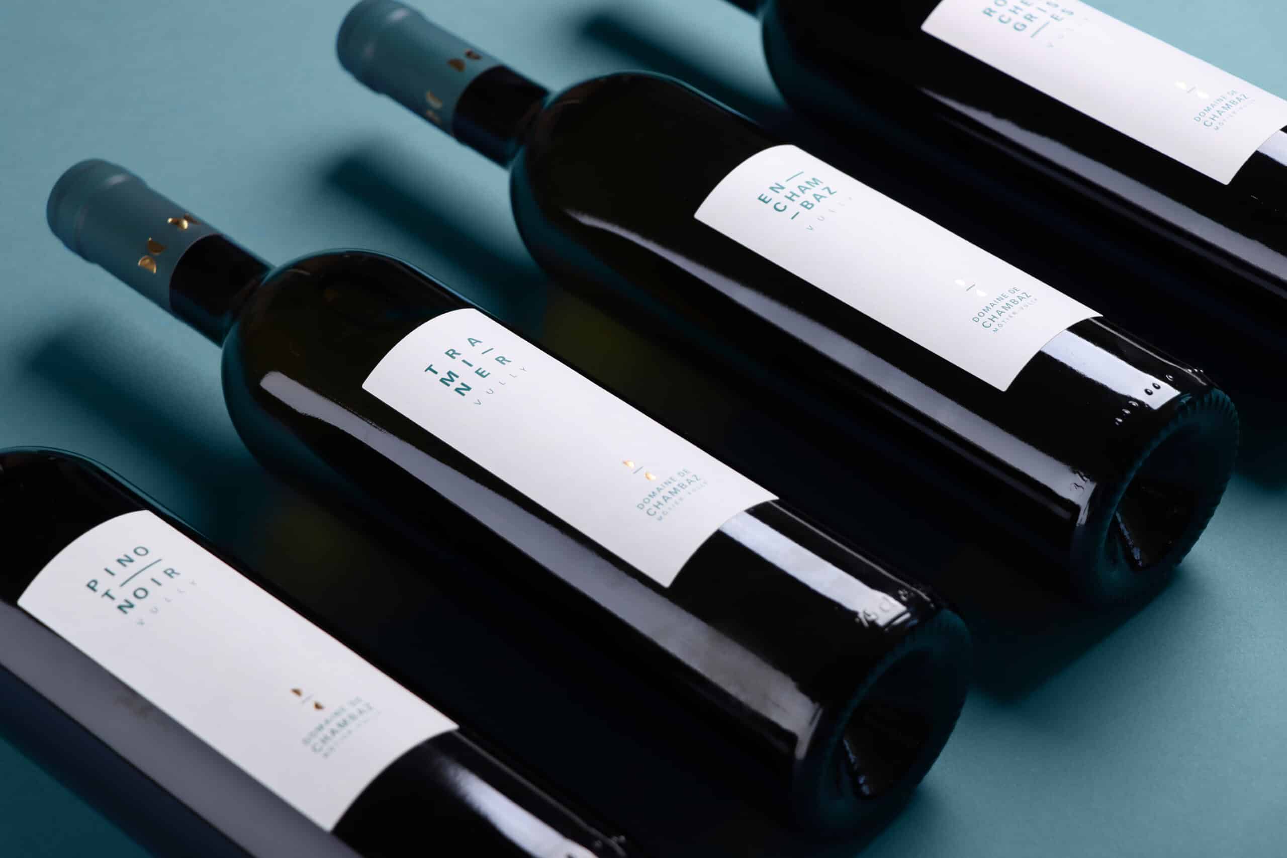 Quatre bouteilles couchées de Pinot Noir, Traminer, En Chambaz et Roches Grises vu en perspective, avec les nouvelles étiquettes Domaine de Chambaz, Môtier-Vully.