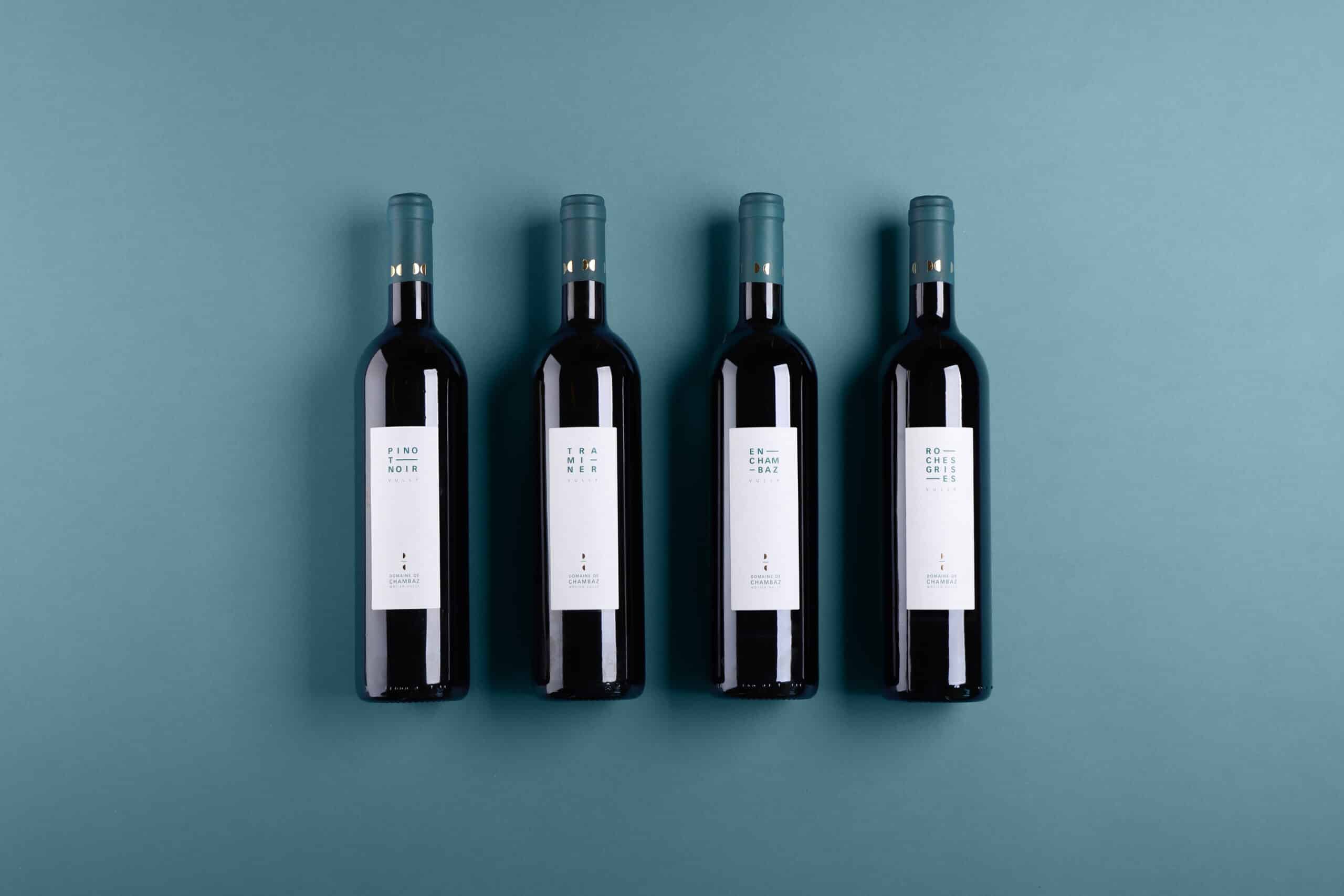 Quatre bouteilles couchées de Pinot Noir, Traminer, En Chambaz et Roches Grises, avec les nouvelles étiquettes Domaine de Chambaz, Môtier-Vully.